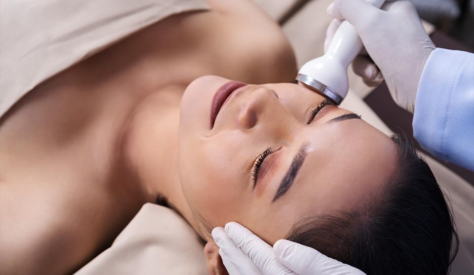 smiling woman having a facial done by a technician wearing gloves one salon facial services